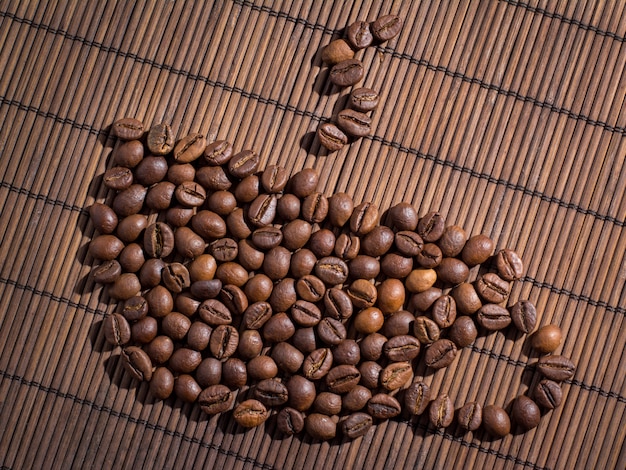 Coffee beans lying on bamboo mat in shape of cup of coffee with fragrant steam