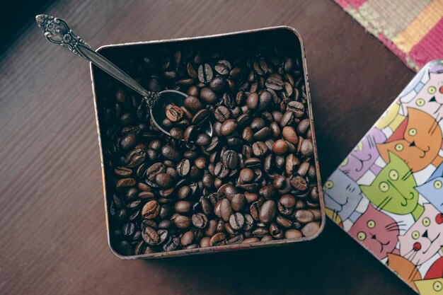 Photo coffee beans in a metal box lie on a brown wooden table top view