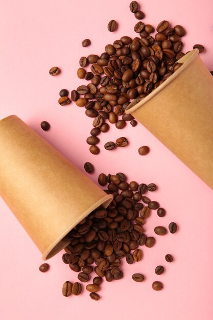 Coffee beans and paper coffee cup on pink background. Top view.