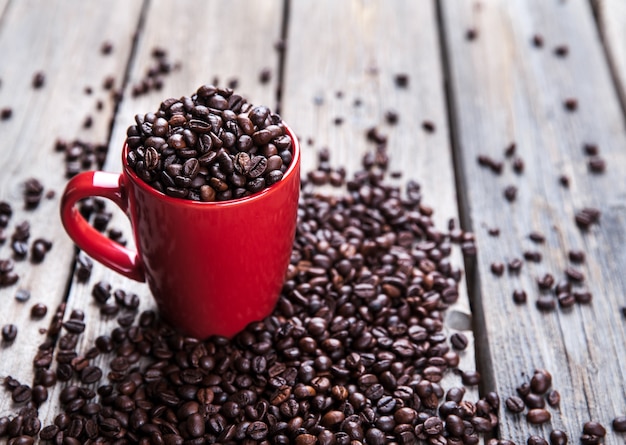 Chicchi di caffè e tazza di caffè rossa sulla tavola di legno.