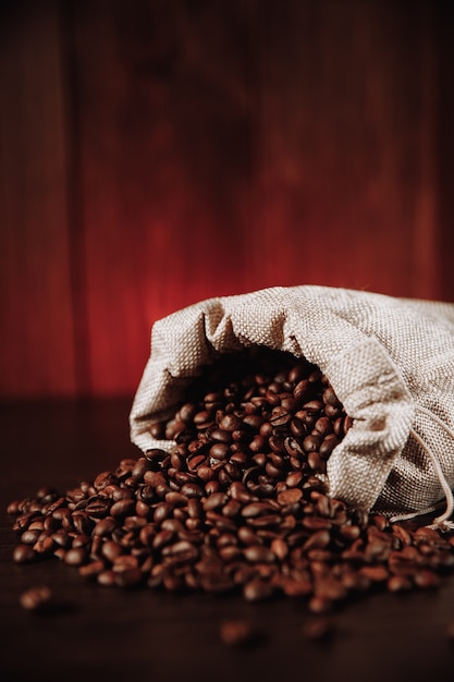 Coffee beans scattered of the bag on wooden table. Vertical image.