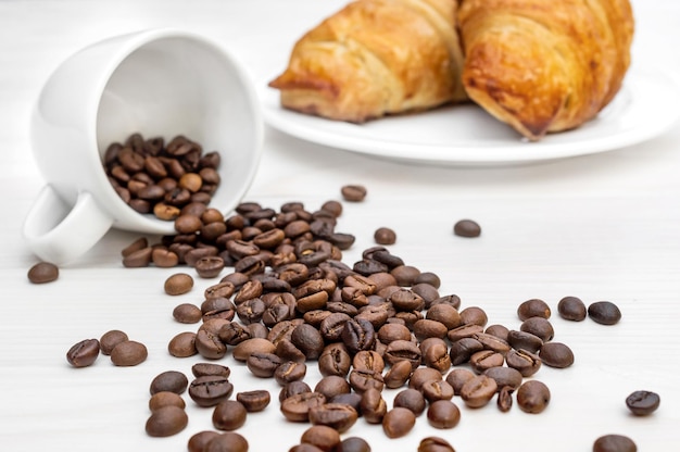 Coffee beans scattered from cup and two croissants on the table