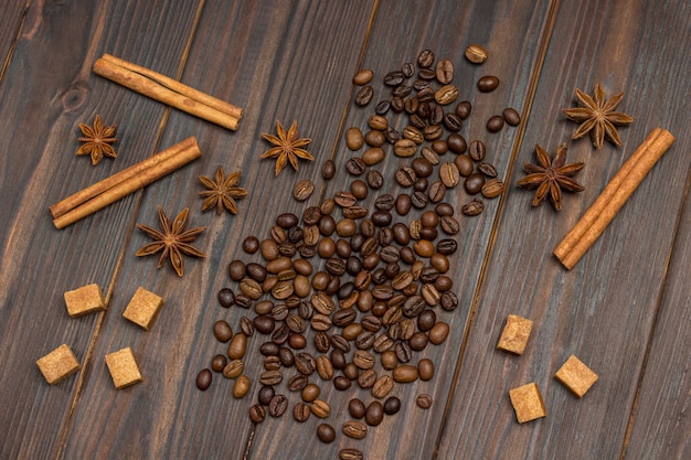 Coffee beans scattered on table, star anise, cinnamon sticks and pieces of brown sugar.