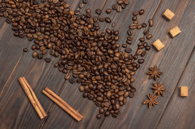 Coffee beans scattered on table, star anise, cinnamon sticks and pieces of brown sugar