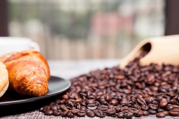 Coffee beans, sweet donut and a cup of coffee in close up photo