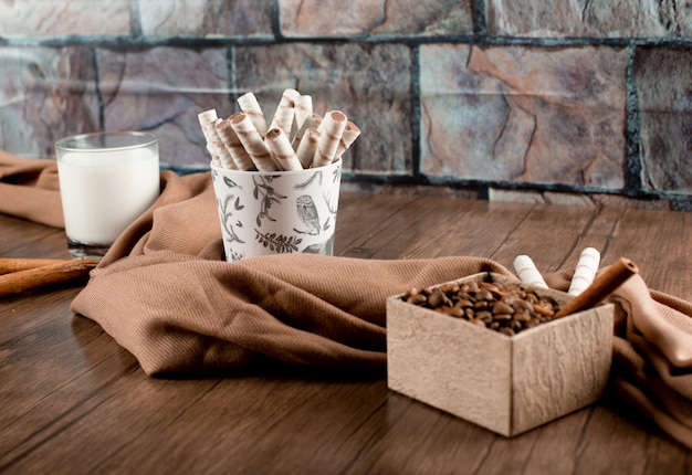 Coffee beans, waffle sticks and a glass of milk wrapped with a scarf on wooden table