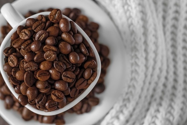 Coffee beans in a white cup on the background of a white knitted scarf