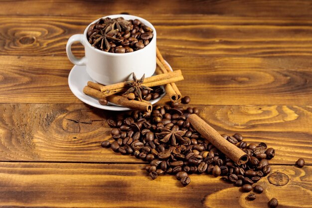 Coffee beans in white cup, cinnamon sticks and star anise on wooden table