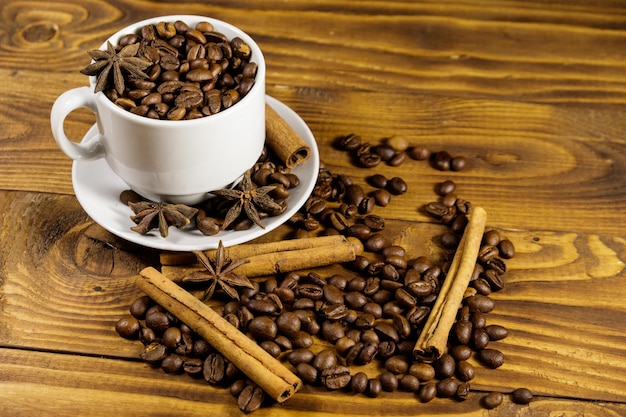 Coffee beans in white cup, cinnamon sticks and star anise on wooden table