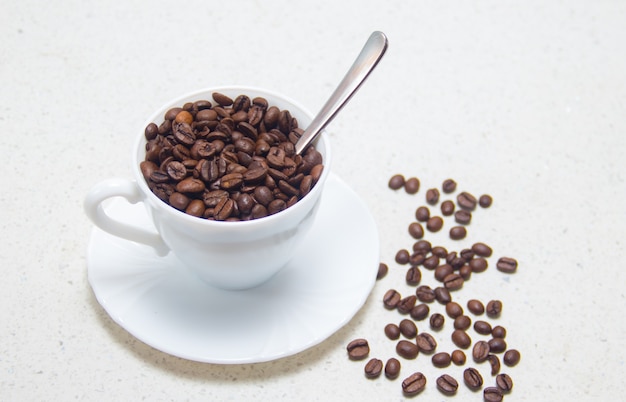 Chicchi di caffè in una tazza bianca. preparazione del caffè. su sfondo chiaro