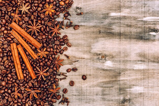 Coffee beans with cinnamon, star anise, cloves spices on rustic wooden texture. Food background vintage toned