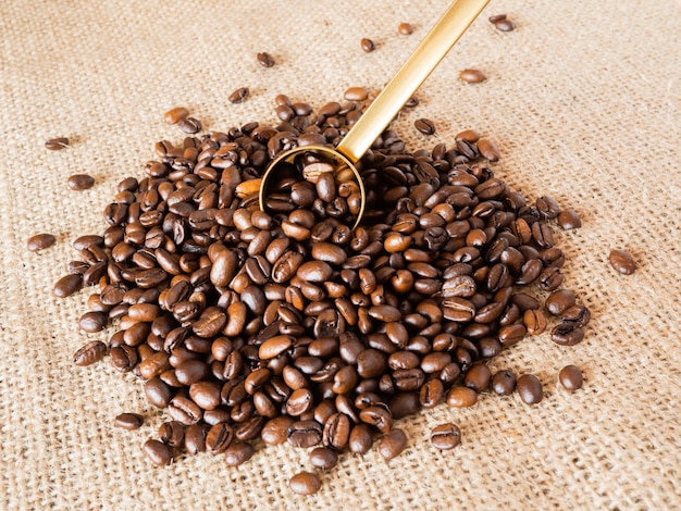 Coffee beans with gold measuring spoon and measuring cup on linen texture background