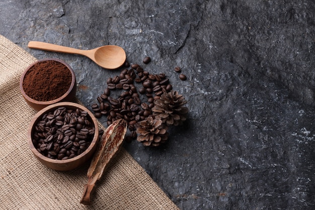 Coffee beans in wooden cup on burlap , wood spoon  on black stone  background