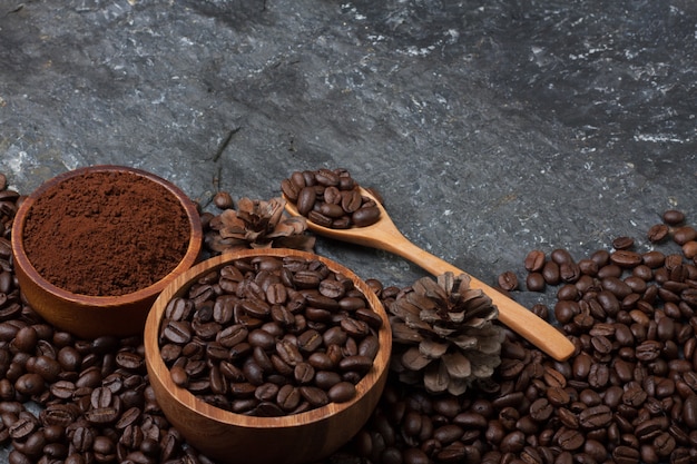 Coffee beans in wooden cup and pine, wood spoon on black stone texture