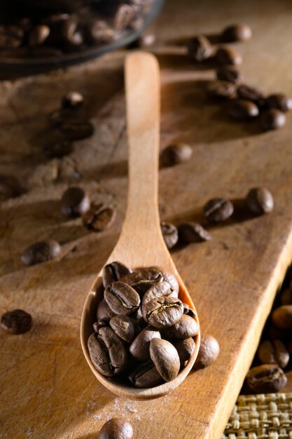 Coffee beans in a wooden spoon on the old wood of the old board