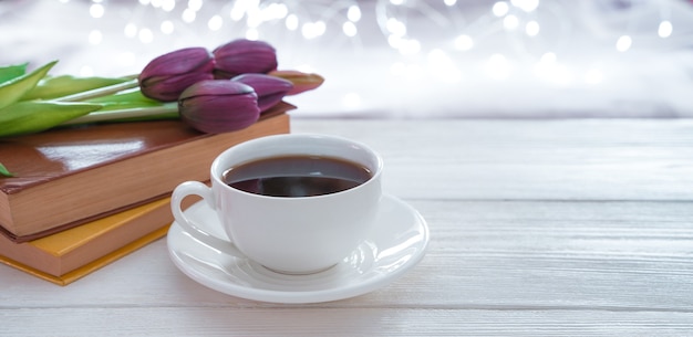 Coffee, books and flowers on a light background with glowing garlands. Side view with copy space