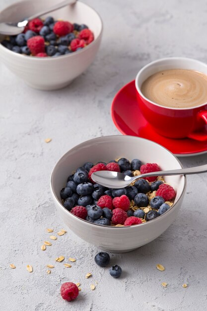 Coffee, bowl of oat flakes with blueberries and raspberries on concrete table.