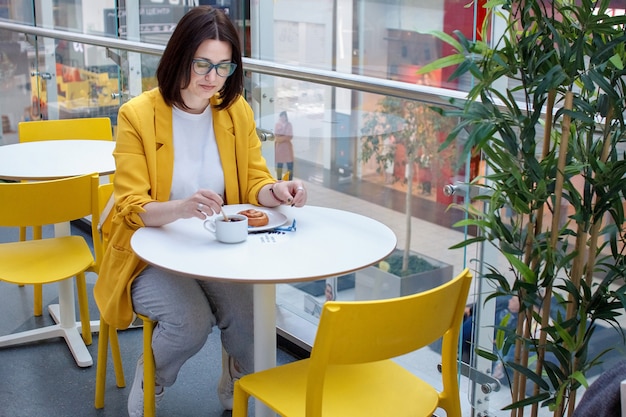 Coffee break. Brunette girl in a yellow jacket with glasses