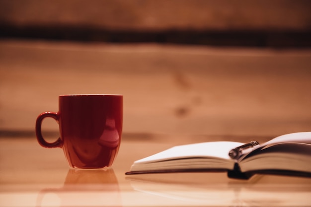 Coffee break. Close-up of coffee cup and notebook on glass table with wooden background