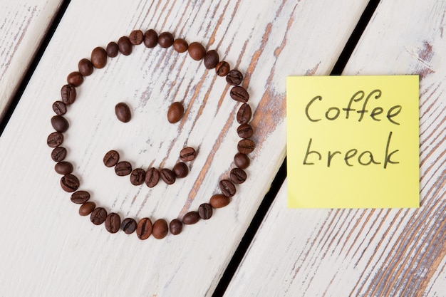 사진 커피 브레이크 개념. 흰색 나무 표면에 웃는 얼굴에 배열하는 커피 콩.