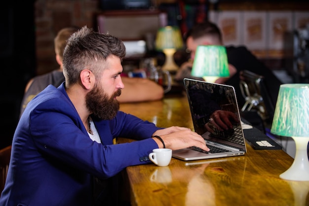 Coffee break concept man bearded businessman sit bar counter
with laptop and cup of coffee create content web blog manager
create post enjoy coffee hipster freelancer work online drinking
coffee