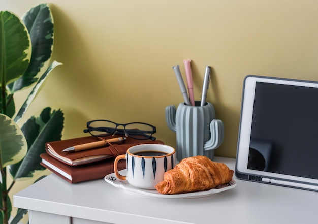 Coffee break in the home office coffee and a croissant on the office table with notebooks tablet and stationery