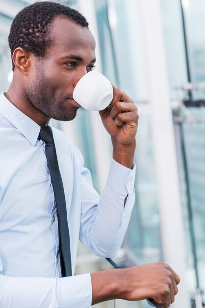 コーヒーブレイク。コーヒーを飲むシャツとネクタイのハンサムな若いアフリカ人の側面図