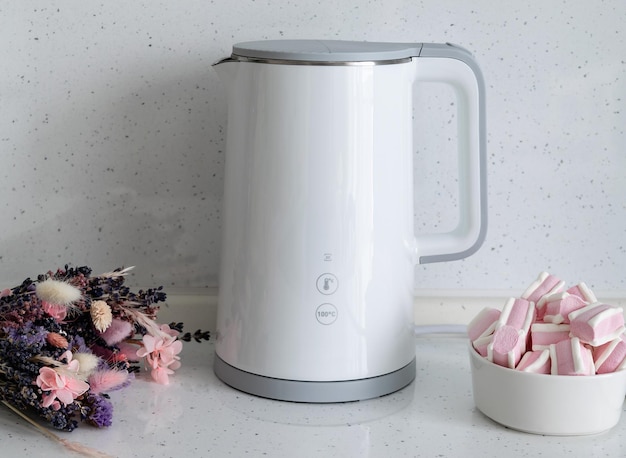 Photo coffee break with sweets. on the countertop of a bright marshmallow kitchen next to a white electric kettle and a bouquet of flowers.