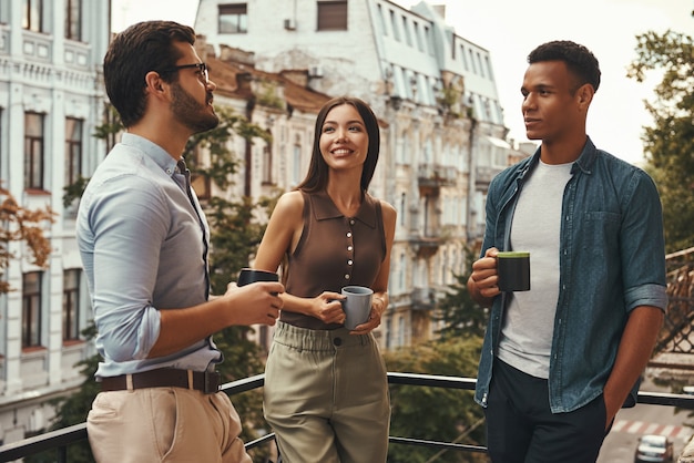 コーヒーブレイク若い陽気な同僚がカップを持って、お互いに話しているカジュアルウェアで