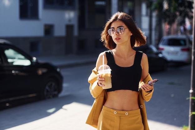 Coffee break Young fashionable woman in burgundy colored coat at daytime with her car