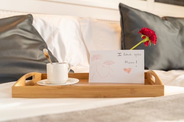 Caffè e colazione preparati su un vassoio con una lettera e un fiore come regalo per la festa della mamma