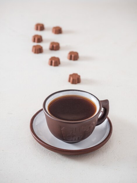 Coffee in a brown mug and curly chocolates on a white table, a coffee break for a sweet tooth