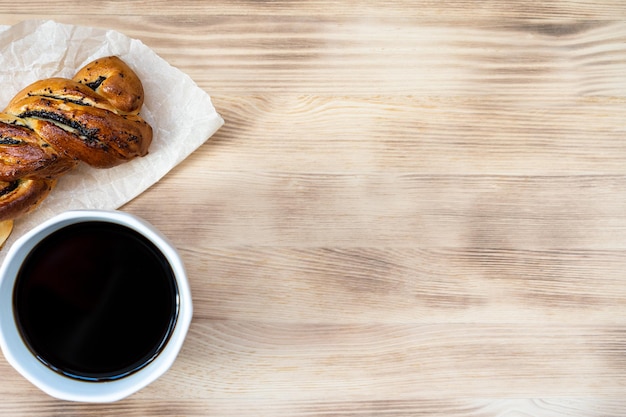 coffee and bun with poppy seeds on wooden background top view space for text