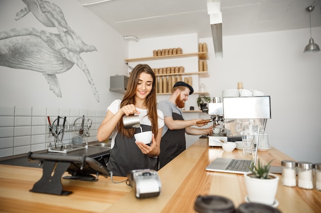 Coffee business concept - primo piano signora barista in grembiule preparando e versando latte in tazza calda, mentre in piedi al caffè.