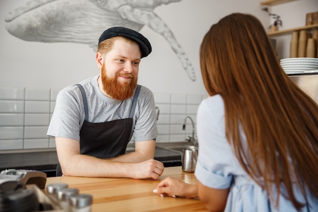 Coffee Business Concept - young beared handsome barista talking with beautiful caucasian customer in modern coffee shop.