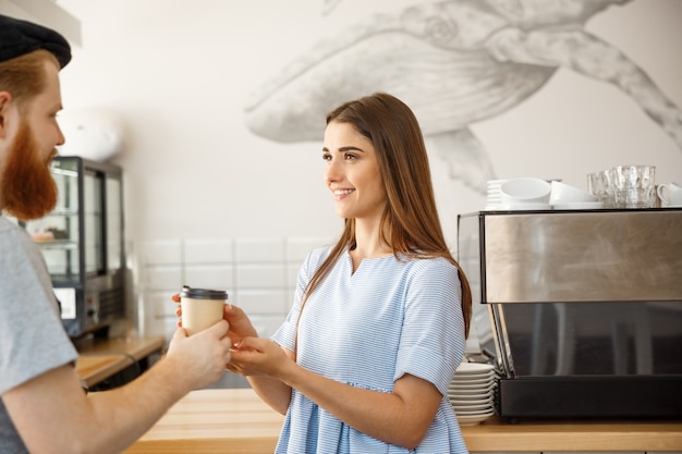 Coffee business concept - il giovane barista a barba elegante godere di parlare e dare tazza di caffè da portare al cliente grazioso.