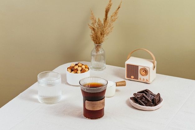 Coffee in a clear glass on the table milk in a milk jug chocolate in a plate