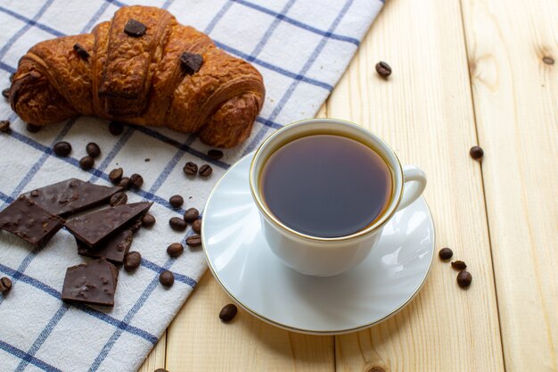 木製の背景にコーヒーとクロワッサン。上からの眺め。コーヒー豆とチョコレート