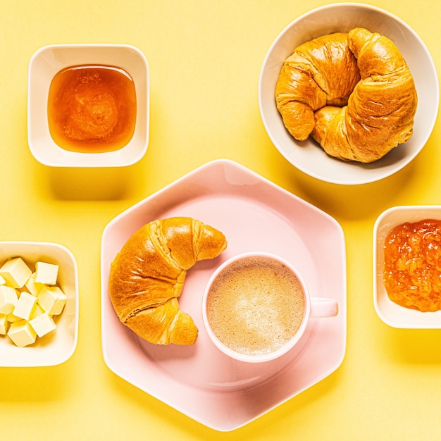 Coffee and croissants for breakfast on a yellow background, top view, flat lay.