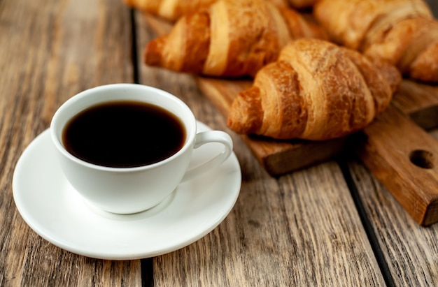 coffee and croissants on a wooden cutting board, on wood background