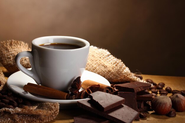 Photo coffee cup and beans cinnamon sticks nuts and chocolate on wooden table on brown background