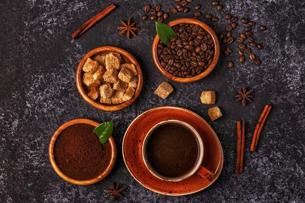 Coffee cup, beans, ground powder and sugar on stone background