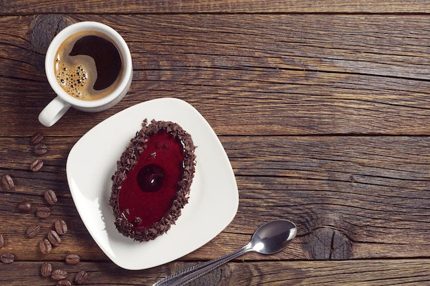 Coffee cup and cake with cherry jelly on dark wooden table, top view