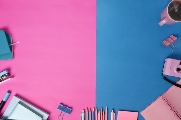 Coffee cup, camera and stationery on two tone blue and pink background.