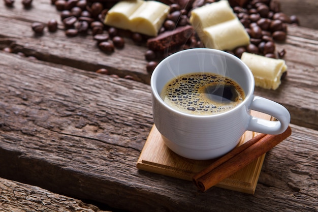 Coffee cup and cinnamon stick. Chocolate and coffee beans. Hot drink served with cinnamon. Simple morning dessert.