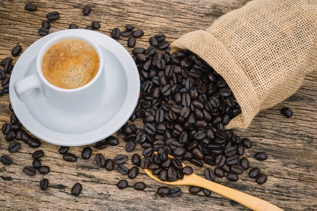 木製の床の袋にコーヒーカップとコーヒー豆の焙煎。