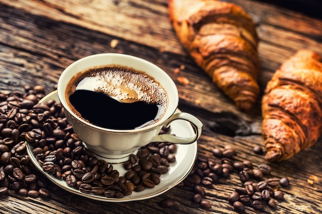 Coffee. Cup of coffee croissants and coffee beans. Vintage cup and old oak table.