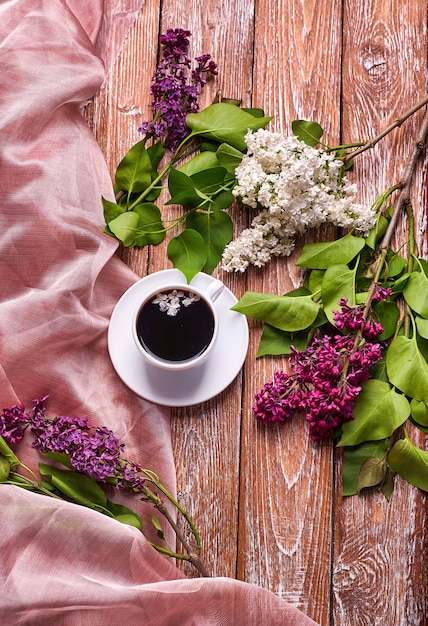 庭の木製テーブルにコーヒーカップと色とりどりのライラックの花。