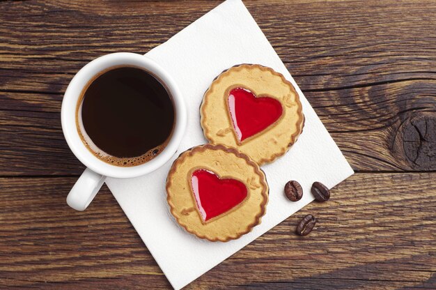 Tazza di caffè e biscotti con giuggiola alla fragola a forma di cuore sul tavolo scuro, vista dall'alto