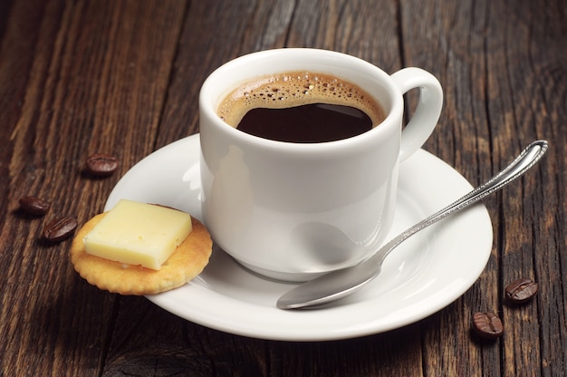 Coffee cup and crackers with cheese on dark wooden table